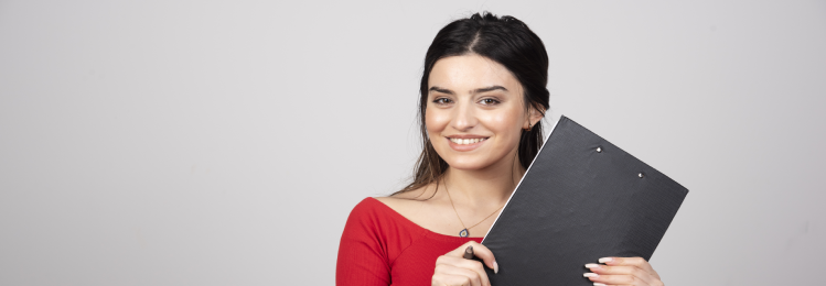Smiling woman in red top holding black clipboard against gray background, showing confidence and professionalism.