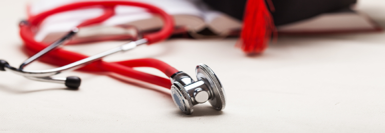 A red stethoscope lies on a table next to an open book with a red tassel, symbolizing medical education and achievement.